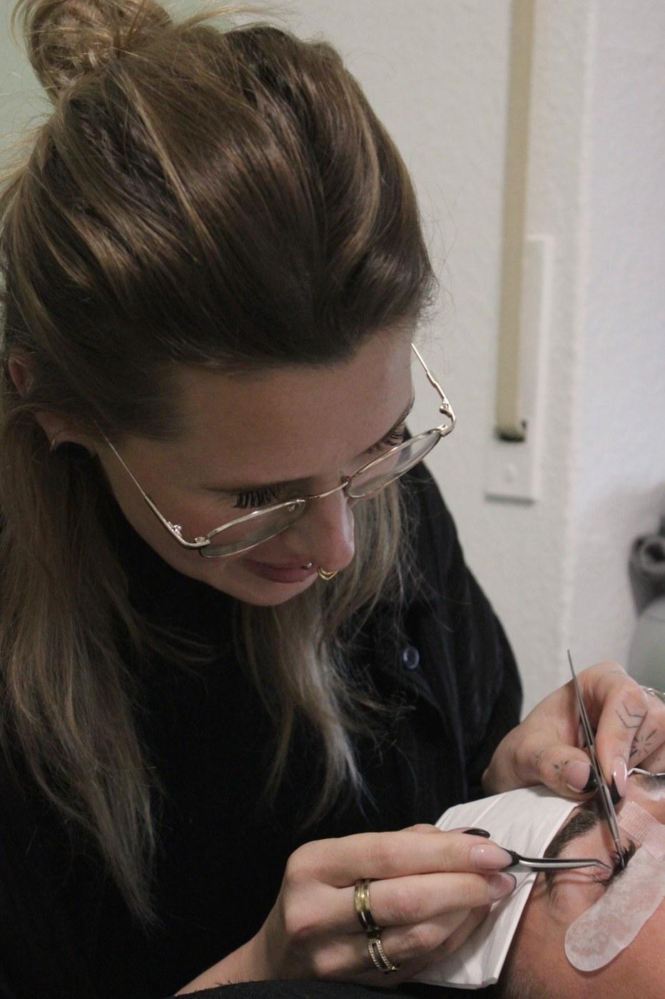 Claudia setzt mit der Pinzette einzelne Wimpern an